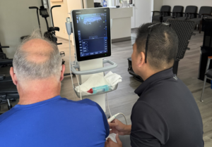 Osteopractic physical therapist using musculoskeletal ultrasound imaging to assess a patient's shoulder pain in a Fishers, IN clinic